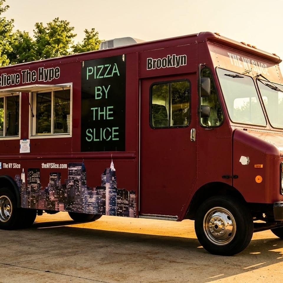 Maroon pizza food truck labeled The NY Slice and Pizza by the Slice parked outdoors, featuring a city skyline mural.