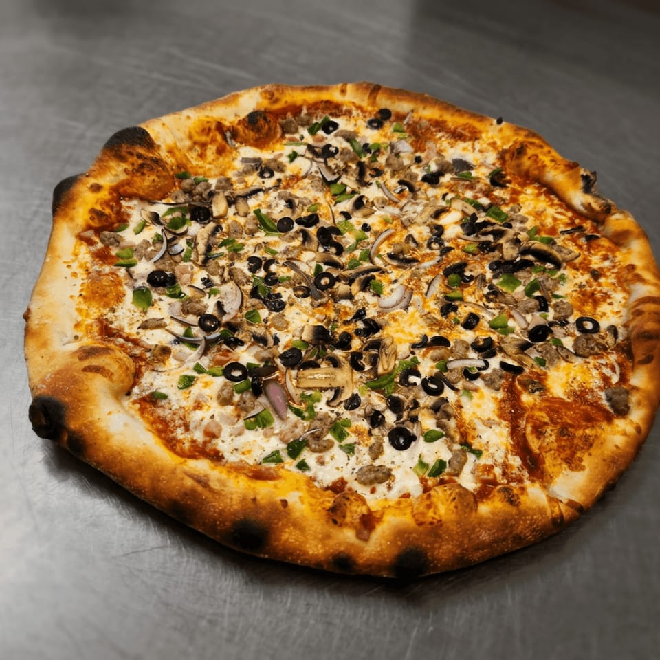Freshly baked pizza topped with mushrooms, black olives, green peppers, onions, and melted cheese on a metal surface.